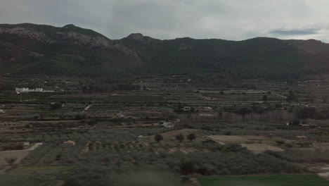 Grüne-Landschaft-Mit-Bergen-Und-Ackerland-Im-Zugfenster