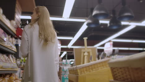 Attractive-girl-customer-is-buying-bread-in-bakery-department-is-shop-smelling-it-smiling-and-putting-in-shopping-trolley.-Healthy-lifestyle-and-supermarket-concept.