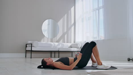 Woman-in-sportswear-doing-hip-bridge-exercise.-Joyful-attractive-young-woman-lying-on-floor-in-living-room-and-doing-hip-bridge-exercise
