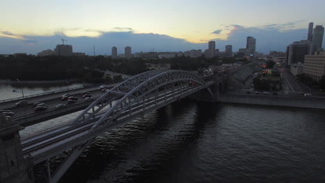 An-evening-view-of-a-railway-bridge-next-to-the-road-bridge-with-an-urbanscape-on-the-background