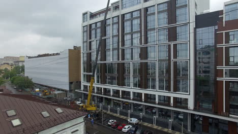 Aerial-view-of-street-with-crane-lifting-glass-panels-on-the-building-top