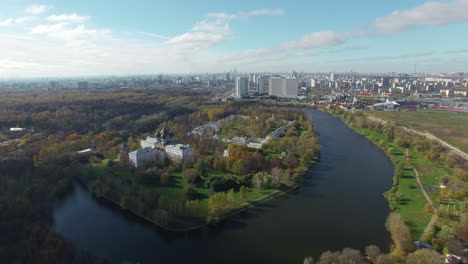 Una-Vista-Aérea-De-Un-Hermoso-Estanque-Entre-árboles-Verdes-Contra-Un-Paisaje-Urbano-Soleado