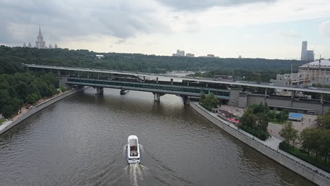 Eine-Luftaufnahme-Von-Moskau-Mit-Einem-Boot,-Das-Durch-Den-Fluss-Schwimmt,-Und-Grünen-Baumkronen-Rundherum