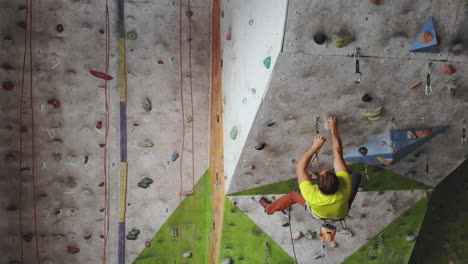 Young-man-Rock-climber-is-Climbing-At-Inside-climbing-Gym.-slim-pretty-man-Exercising-At-Indoor-Climbing-Gym-Wall.