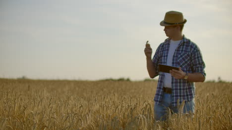 Granjero-Que-Usa-Tableta-En-Campo-De-Trigo.-Científico-Que-Trabaja-En-El-Campo-Con-Tecnología-Agrícola.-Cerca-De-La-Mano-Del-Hombre-Tocando-Tablet-Pc-En-Tallos-De-Trigo.-Agrónomo-Investigando-Espigas-De-Trigo