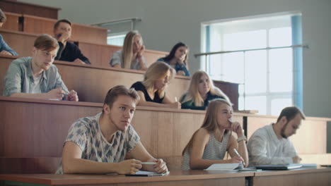 Modern-students-men-and-women-sit-at-desks-in-a-large-classroom-and-write-a-lecture-notes.-Get-an-education-for-a-successful-career