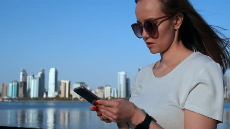 Una-Chica-Con-El-Pelo-Largo-Marca-Un-Mensaje-En-El-Teléfono-Inteligente-En-El-Muelle-De-Dubai