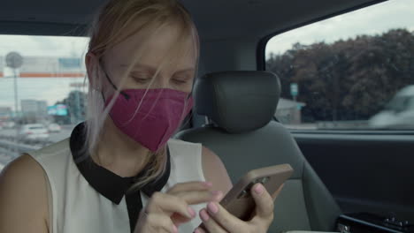 Weiblicher-Taxifahrer-Mit-Maske,-Der-Auf-Dem-Handy-Im-Internet-Surft