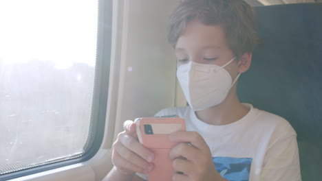 Niño-Con-Máscara-Viajando-En-Tren-Y-Usando-El-Teléfono