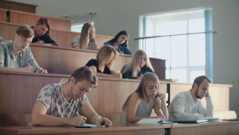 Young-men-and-women-sitting-in-a-university-or-college-classroom-write-a-lecture-with-a-pen-and-using-a-laptop.-Institute-education