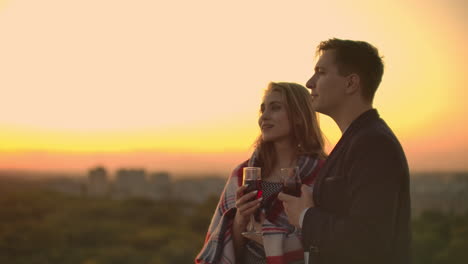 Amantes-Abrazando-A-Una-Chica-Mirando-La-Puesta-De-Sol-Con-Vino-Parado-En-El-Techo-Del-Edificio.-Imagen-En-Cámara-Lenta-De-La-Relación-De-Una-Joven-Pareja-Casada.