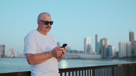 Bearded-senior-man-standing-outdoors-using-smartphone.-Retired-male-reading-news-chatting-with-his-children-via-mobile-phone.-Studying-city-map-app.-Lost-in-city-looking-for-right-direction.