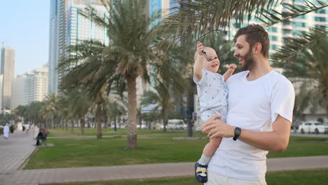 Padre-Jugando-Con-Sus-Hijos-En-El-Verano-En-Una-Ciudad-Moderna-Abrazándolo-Y-Abrazándolo-Con-Una-Camiseta-Blanca-Y-Pantalones-Cortos.