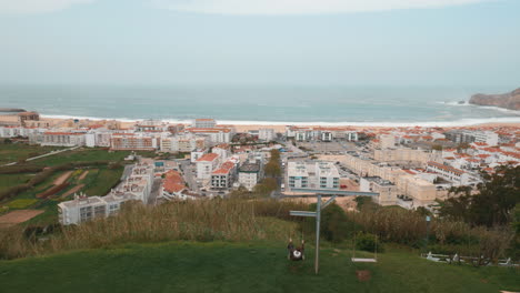 Chico-Balanceándose-Y-Observando-La-Ciudad-Turística-Costera-De-Nazaré,-Portugal