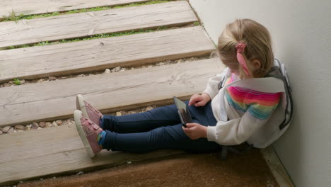 Child-with-phone-waiting-at-house-entrance-and-sitting-on-wooden-path