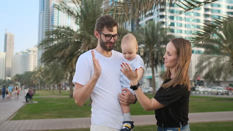 Mom-father-and-son-standing-in-the-Park-smiling-and-hugging-looking-at-each-other-in-the-summer-among-the-palm-trees