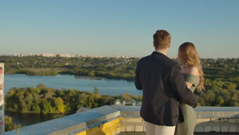 Young-couple-in-love-standing-on-the-roof-hug-and-closely-look-at-each-other.-Romantic-evening-on-the-roof-of-the-building.-A-date-on-the-roof-of-a-building-love.-Slow-motion