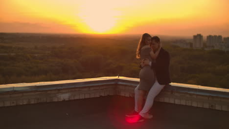 Lovely-sweet-happines-couple-sit-on-the-roof-top-with-amazing-sunset-view-on-the-urban-city-town.-They-love-each-other-hugs-very-tenderness-sun-goes-between-hair