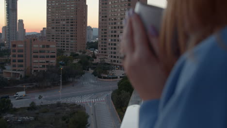 Woman-drinking-tea-and-looking-at-morning-city-from-the-balcony