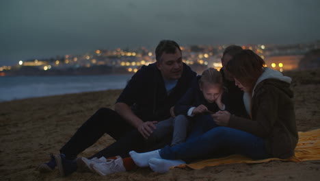 Family-watching-phone-on-ocean-shore