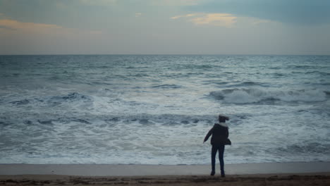 Teenage-boy-dancing-on-ocean-beach-at-dusk