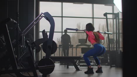 La-Deportista-Con-Top-Rosa-Y-Leggins-Azules-Se-Prepara-Para-Competiciones-Importantes.-Ella-Está-Haciendo-Sentadillas-Con-Una-Barra-Vacía-Con-Una-Técnica-Correcta.