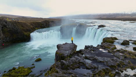 View-Of-A-Man-Standing-On-A-Cliff-In-Godafoss-Waterfall,-Iceland---Aerial-Drone-Shot