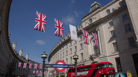 Autobús-De-Dos-Pisos-En-El-Cruce-De-Carreteras-De-Piccadilly-Circus-Con-Banderas-Del-Reino-Unido-Colgando-Sobre-Regent-Street-En-Londres,-Reino-Unido