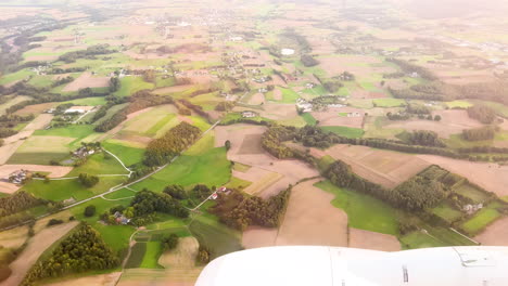 Aerial-view-of-the-lush-countryside-from-an-airplane-window,-showcasing-the-patchwork-of-fields-and-farmlands