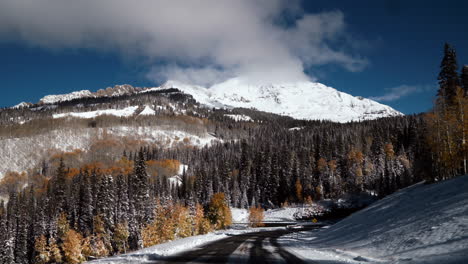 Driving-frosted-snow-road-crisp-cold-freezing-frozen-morning-shaded-Kebler-Pass-Colorado-aerial-cinematic-drone-shaded-fall-winter-season-collide-red-yellow-orange-aspen-tree-forest-forward-pan-up