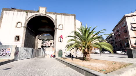 Porta-Capuana-In-Neapel,-Ein-Antikes-Stadttor,-Präsentiert-Die-Reiche-Geschichte-Und-Architektur-Unter-Einem-Strahlend-Blauen-Himmel,-Wobei-Eine-Markante-Palme-Den-Mediterranen-Charme-Der-Szene-Unterstreicht