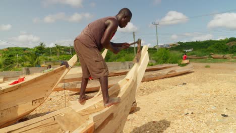 Hombre-Africano-Tallando-Proa-De-Barco-De-Madera-Con-Azuela-En-El-Astillero-Del-Pueblo