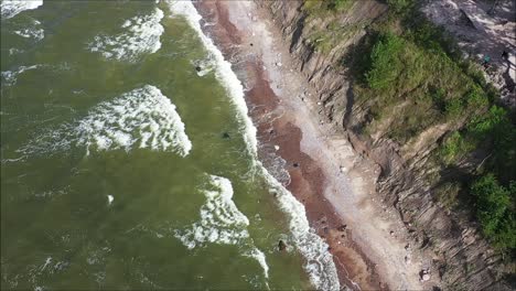 Unearthing-the-allure-of-a-high-cliff-coastline-along-the-Baltic-Sea-in-Lithuania,-a-drone-captures-the-dynamic-spectacle-of-large-waves-and-the-mesmerizing-green-waters-with-moody-undertones