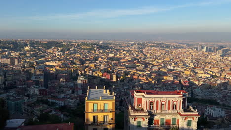 Panoramic-cityscape-of-Naples-at-dusk,-with-buildings-bathed-in-the-warm-glow-of-the-setting-sun-and-the-Vesuvius-volcano-in-the-backdrop