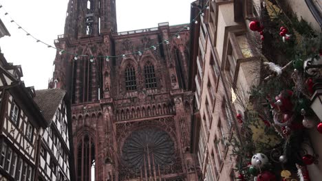 panning-up-shot-of-strasbourg-cathedral-and-tall-bell-tower-with-christmas-decorations-at-Festive-Christmas-market-in-Strasbourg,-France-Europe