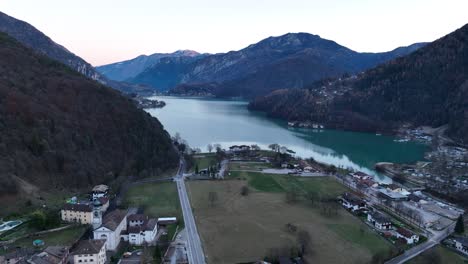 Aerial-Lateral-Drone-shot-of-Pieve-di-Ledro-and-Ledro-Lake-with-car-crossing-bridge-on-Massangla-River
