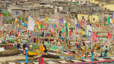 Flags-flap-in-wind-on-boats-in-busy-fishing-harbor,-Cape-Coast,-Ghana