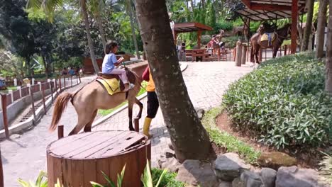 Little-Girl-ride-horses-guided-by-staff-at-a-playground-in-the-countryside,-Semarang,-Central-Java