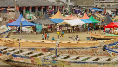 People-by-fishing-boats-and-market-tents-at-Cape-Coast-in-Ghana,-wide