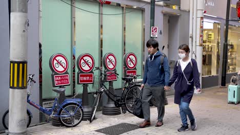 Japanisches-Paar,-Das-An-Einer-Reihe-Von-Fahrradverbotsschildern-Auf-Der-Straße-In-Osaka-Vorbeigeht