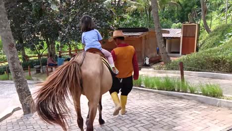 Girl-riding-horses-guided-by-staff-at-a-playground-in-the-countryside,-Semarang,-Central-Java