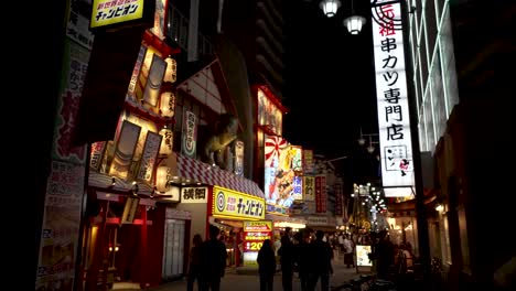 Silhouette-Von-Menschen-Entlang-Der-Straße-Im-Shinsekai-Viertel,-Beleuchtet-Durch-Leuchtreklamen-In-Der-Nacht-In-Osaka