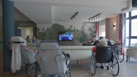 Grupo-De-Mujeres-Mayores-En-Sillas-De-Ruedas-Viendo-Televisión-En-Un-Centro-De-Atención-Para-Personas-Mayores