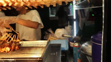 Asian-hawker-flip-meat-of-skewered-crocodile-broiling-on-grill-at-street-food-market