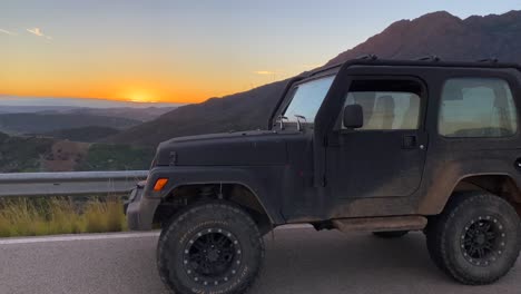 Jeep-Negro-4x4-Y-Hermosa-Puesta-De-Sol-Naranja-Con-Vista-A-Sierra-Bermeja,-Divertidas-Aventuras-En-Vehículos-Todo-Terreno-En-Marbella-Málaga-España,-Toma-De-4k