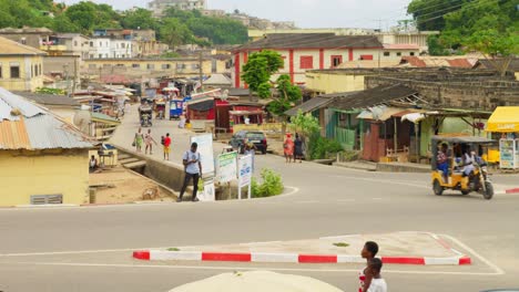 Everyday-street-traffic-by-simple-houses-and-trees,-Cape-Coast,-Ghana