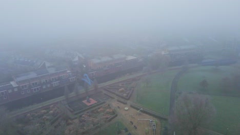 Luftaufnahmen-Eines-Wunderschönen-Grünen-Parks-In-Einem-Vorstadtviertel,-Der-Von-Nebel-Bedeckt-Ist