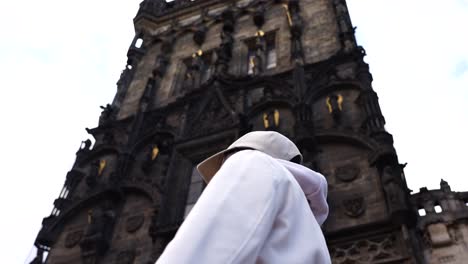 Female-tourist-stand-and-turn-toward-tall-Powder-Tower-gothic-facade,-Prague