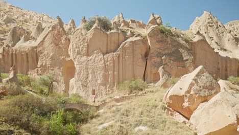 Female-tourists-walks-over-stone-arch-bridge-dramatic-landscape-trail