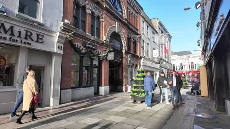 Pedestrians-in-winter-coats-and-jackets-with-coffee-mug,-in-slow-motion-on-the-street-of-Cork-City,-Ireland-sunny-morning